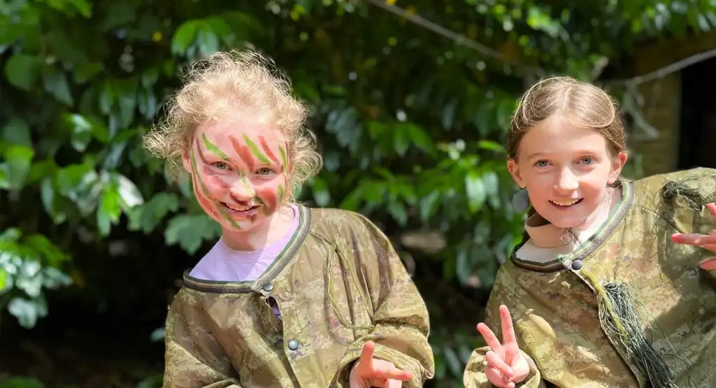 A group of children cheering and celebrating after reaching the top of a rock wall at Fota Island Adventure, surrounded by lush greenery