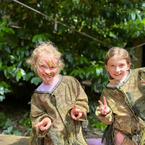 A group of children cheering and celebrating after reaching the top of a rock wall at Fota Island Adventure, surrounded by lush greenery