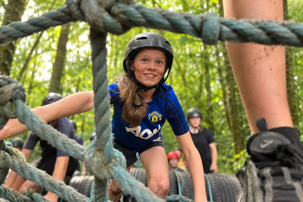Child wearing a helmet climbing through a rope obstacle in the woodland at Fota Adventure