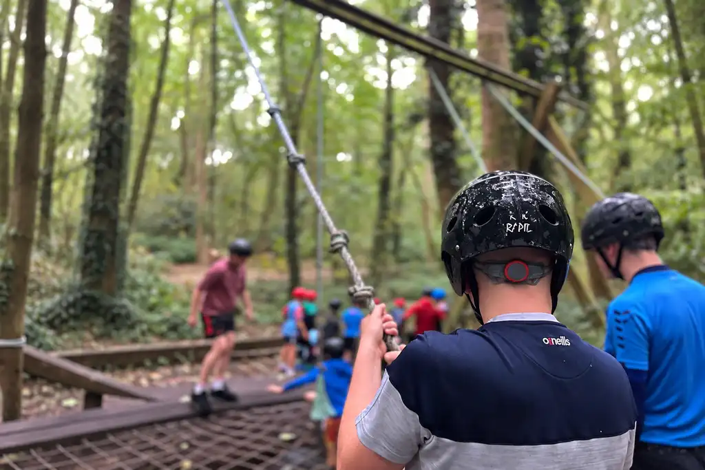 Child wearing a helmet taking part in an aerial obstacle course in the woodland at Fota Adventure